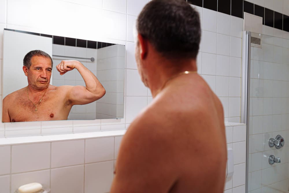 Man in bathroom looking at himself in mirror and flexing biceps